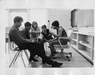Five students in a classroom looking at a document [ca. 1955-1976]