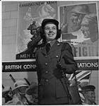 Service féminin de l'Armée, à Ottawa. Une femme souriante, en uniforme. Des affiches de la nouvelle Armée canadienne en arrière-plan December 1941