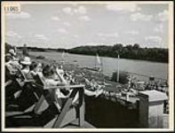 Men and women seated on deck chairs at the Winnipeg Canoe Club, on the banks of the Red River 1944