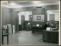 La préposée au prêt, Barbara Morphy, aide deux clients dans la salle principale de la Bibliothèque publique de London en Ontario March 1945