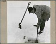 Un homme perce un trou dans la glace pour y pêcher March 1945