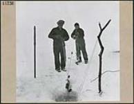 Two men lower nets from a hole to hole in the ice March 1945