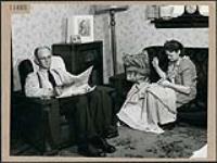J. W. (Ed) Maddocks lisant le journal dans sa salle de séjour pendant que son épouse coud, à Toronto April 1945