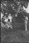Wilson P. MacDonald reading to a group of people under a tree [1925]
