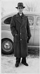 Wilson P. MacDonald debout devant une voiture, portant un pardessus [1940]
