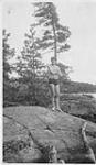 Wilson P. MacDonald wearing a swimsuit and standing on a rock [1925]