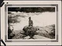 Woman sitting on a rock in front of rapids [1925]