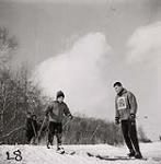 [Young boy wearing a winter hat sets off down a hill skiing as a male instructor watches] [between 1953-1964]
