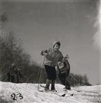 [Young girl with her hood up and tongue out, sets off down a hill skiing as a male instructor watches] [between 1953-1964]
