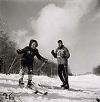 [Young girl with snow on her pants, sets off down a hill skiing as a male instructor watches] [between 1953-1964]