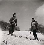 [Young boy sets off down a hill skiing as a male instructor watches] [between 1953-1964]
