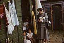 Femme prenant des notes à côté de trois enfants autochtones assis dans une entrée, Port Edgar Cannery n.d.