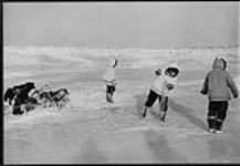 Infirmière sur la glace à Chimo avec deux hommes portant des parkas et accompagnés d'une meute de chiens 1954