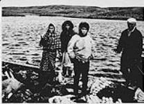 Quatre Inuits debout au bord de l'eau avec leur prise (?) n.d.