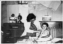 Miss Marion Tomatick sitting on her bed with her young son, Moose Factory septembre 1969