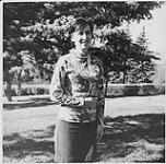 Graduate of the Community Health Worker Training Program in Fort San Saskatchewan Ms. McGregor, standing in a park [ca 1970]
