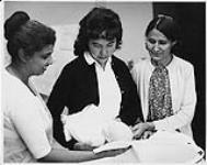 The proper way to hold and bath an infant is shown to students. Lucy Isaac of Hay River, N.W.T. is holding the child as Miss S. Kuruvilla instructs and Dora Gully of Fort Franklin looks on n.d.
