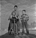 Homme avec fillette sur un vélo et garçon debout près d'eux, Brandon, Manitoba 1954