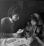 Theresa Billette, age 15, and her sister, Delia, aged five, stitching beads on moosehide moccasins. [They are from the Buffalo River Dene First Nation at Dillon, Saskatchewan.] 19 mars 1955