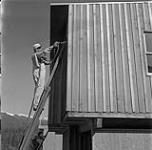 Homme peinturant une maison, Kitimat, Colombie-Britannique juin 1956.