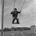 Boy standing on a swing, Swan River, Manitoba June 23, 1956.