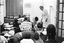 Infirmière s'adressant à un groupe de femmes agenouillées [ca.1954-1963]