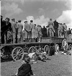 People standing on wagons while others lounge on the grass in the foreground [ca.1954-1963]