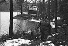 Homme portant un chapeau Esso debout dans la forêt [ca.1954-1963]