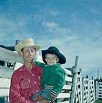 Cowboy tenant un garçon dans ses bras au rassemblement de bétail de Swan River, Manitoba June 30, 1956.