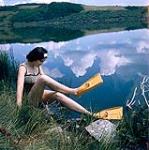 Female scuba diver Heather McEwen sitting at water's edge wearing yellow flippers 1954