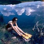 Female scuba diver Heather McEwen seated at water's edge wearing yellow flippers 1954