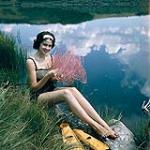 Female scuba diver Heather McEwen sitting at water's edge holding a pink fan coral 1954