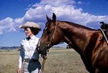 Cowgirl standing and holding horse's reigns September, 1962