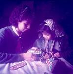 Theresa Billette, âgée de 15 ans, et sa soeur, Delia, âgée de 5 ans, cousant des billes sur des mocassins en peau d'orignal, Dillon, Saskatchewan [Elles sont de la Première nation des Dénés de Buffalo River à Dillon (Saskatchewan).] March 19, 1955.