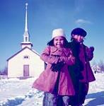 Two girls standing outside, Southend, Saskatchewan [Rose Anne Hardotte (née Jobb) on the left and Jane McCallum (right) from the Peter Ballantyne Cree Nation] March 1955.