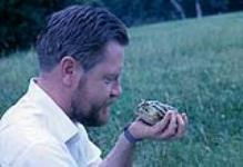 Profile portrait of Gerald Durrell holding a frog. Channel Island Zoo. Jersey [ca 1953-1964]
