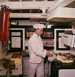Galley cook of the M.V. Christmas Seal, Cyril Sturge, taking bread out of the pans. Newfoundland. août 1960