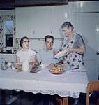An interior of the farm kitchen showing the family seated at the table. Quebec.  [L'intérieur d'une cuisine de ferme où l'on voit la famille assis à la table. Québec.] 1957