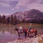 [Homme et femme, à cheval au bord d'une rivière, Alberta] August 1956