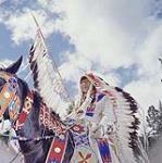 A Stoney Nakoda First Nation man [Frank Crawler] on horseback wearing a long feathered headdress and some beaded clothing  during "Banff Indian Days", Alberta août 1957