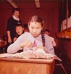 An Inuit girl painting a sculpture on her desk at school, Frobisher Bay, Northwest Territories [Iqaluit (formerly Frobisher Bay), Nunavut] mai 1958.