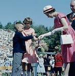 Her Majesty Queen Elizabeth receiving a bouquet of roses from the children of London, Ontario, while Mayor J. Allan Johnston looks on. July 1959