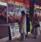 The display window of a butcher's shop in the Farmers' Market in Ottawa. There are several signs showing the various prices of the cuts of meat. Ottawa, Ont. 1961