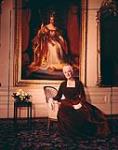 Madame Vanier (Pauline Archer) seated in front of a large painting of Queen Victoria n.d.