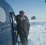 Man in uniform speaking into two-way radio outside van, Northern Canada. [Homme en uniforme parlant dans un appareil radio bidirectionnel à l'extérieur d'un fourgon, au nord du Canada.] 1961