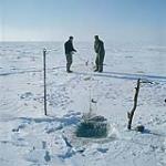 Ice fishermen on Lake Manitoba pulling the net out of the hole across the ice to remove the fish. [Deux hommes hissant un filet de pêche hors d'un trou dans la glace au Lac Manitoba.] février 1961.