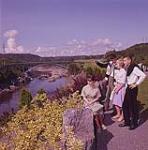Two young men and two young women looking at river from high land. July 1961