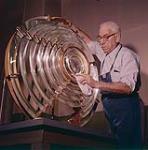 Polishing the lens of a big coastal unit is Bernie McGrory of Prescott, Ontario.  [Bernie McGrory polissant le verre d'une lanterne de voie maritime à Prescott, Ontario.] mars 1961