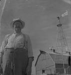 Saskatoon et blé, fermier non identifié à l'extérieur de sa grange [between 1939-1951].
