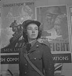 Service féminin de la Force aérienne, années 1940. Femme non identifiée en uniforme devant les nouvelles affiches de l'armée du Canada [between 1940-1949]